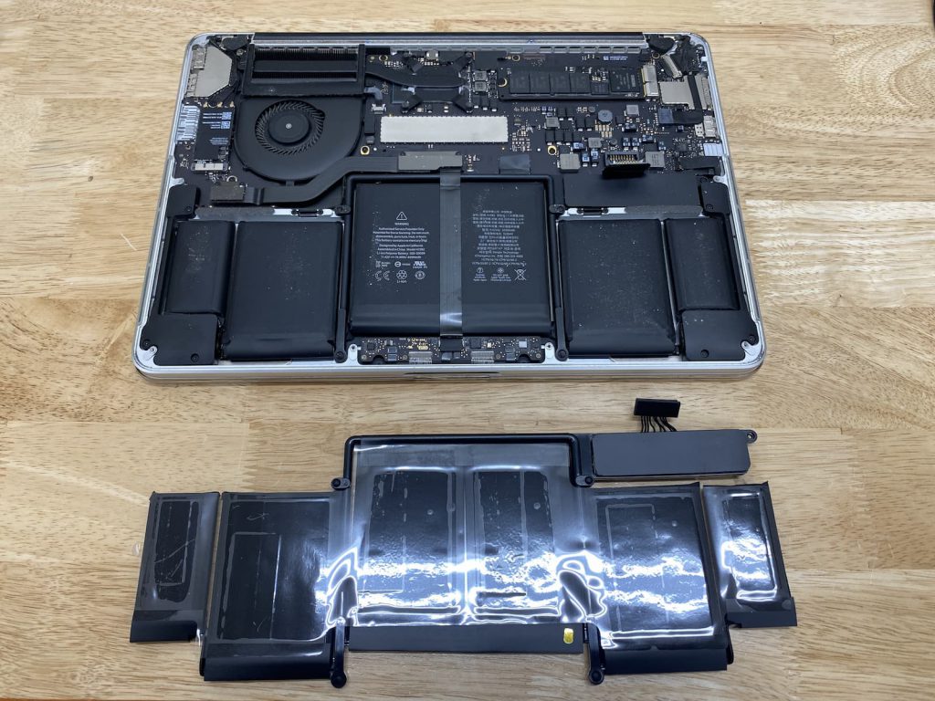 13 inch Macbook Pro with swollen battery next to new battery waiting to be installed.